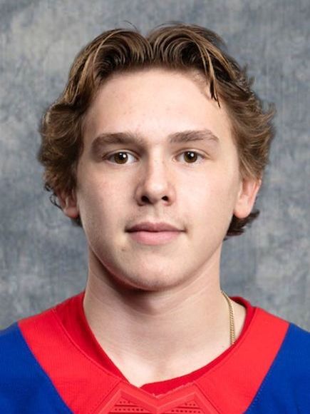 Portrait of a young male hockey player with short, light brown hair, wearing a red and blue hockey jersey.